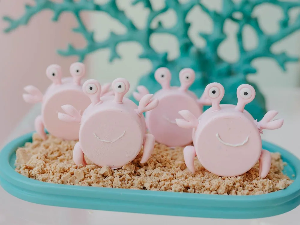 Docinhos de caranguejo rosa sobre farofa de biscoito em festa tema fundo do mar