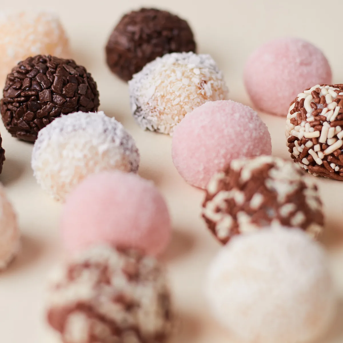 Fileiras de brigadeiros artesanais sortidos da Momento Cake sobre fundo creme