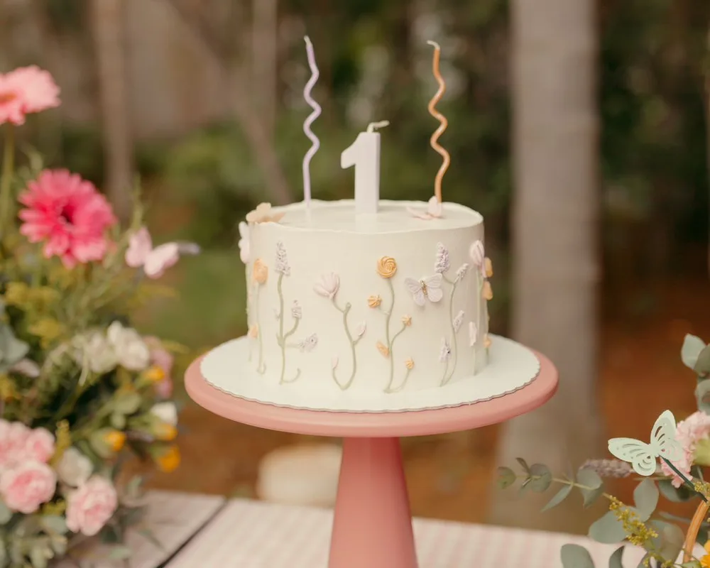 Bolo branco floral de primeiro aninho em suporte rosa em festa no jardim