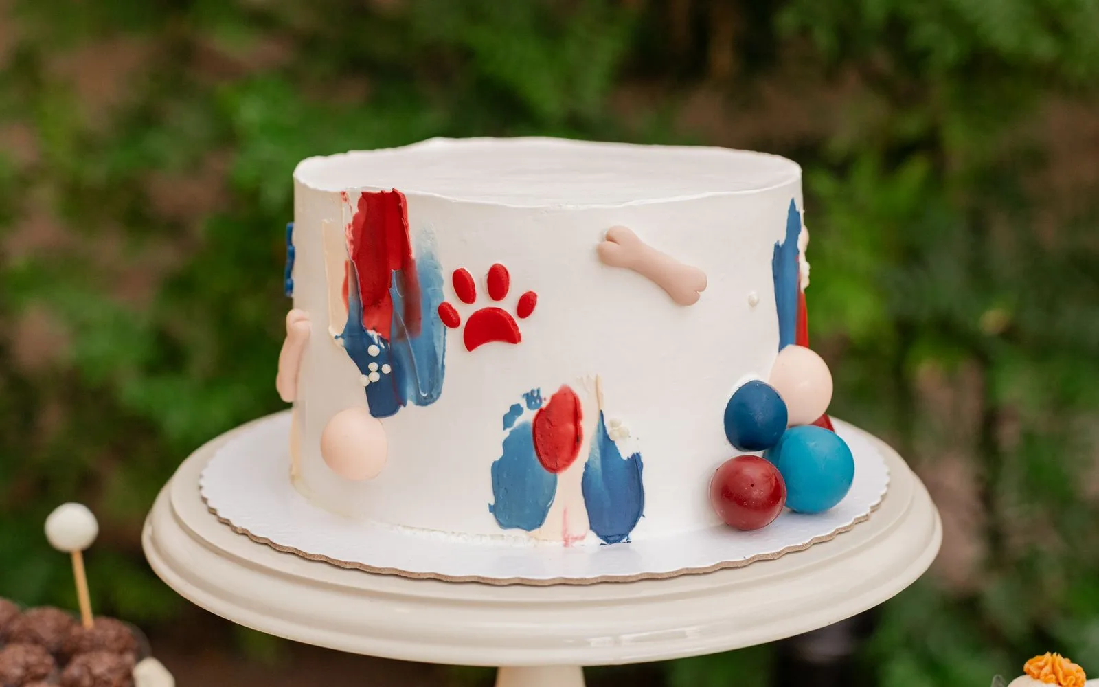 Bolo branco de festa com pinceladas coloridas, patinha e ossinhos em tema cachorrinho